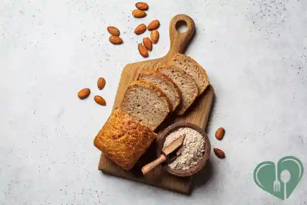 Sliced low-carb almond flour bread on a wooden board with scattered almonds