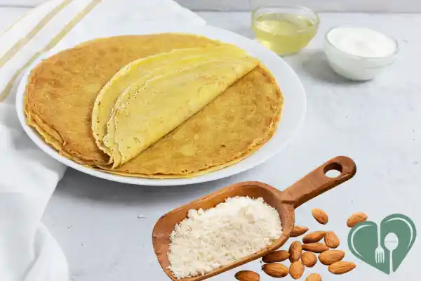 A plate of almond flour pancakes with a scoop of almond flour and whole almonds, next to bowls of yogurt and oil.