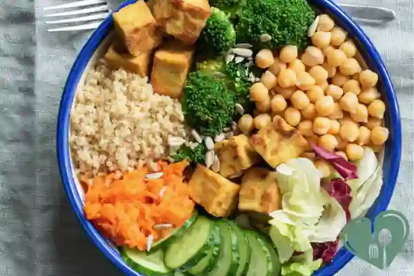 Colorful vegetarian nourish bowl with tofu, chickpeas, quinoa, broccoli, shredded carrot, cucumber, and lettuce.
