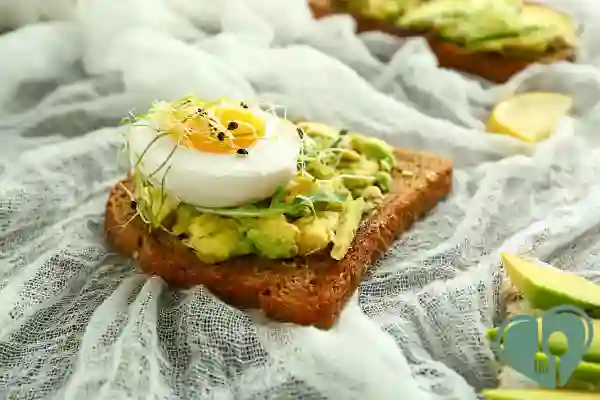 Avocado toast topped with poached egg and microgreens on whole grain bread
