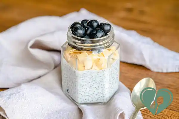 Glass jar of almond chia pudding topped with toasted coconut flakes and fresh blueberries — a low-carb, high-fiber vegan breakfast for diabetics.