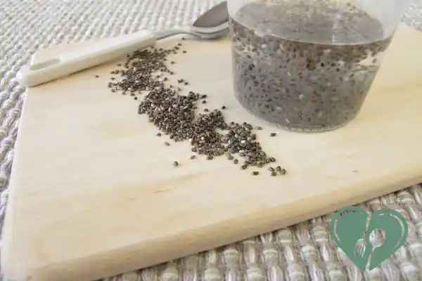 Dry chia seeds scattered on a wooden board next to a glass of soaked chia gel — a natural binder used in low-carb diabetic baking.
