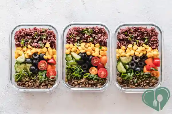 Three glass containers with brown rice, lentils, corn, cucumbers, tomatoes, and olives.