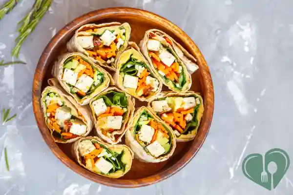 Assorted vegan tofu wraps with fresh vegetables, arranged in a wooden bowl, top view.