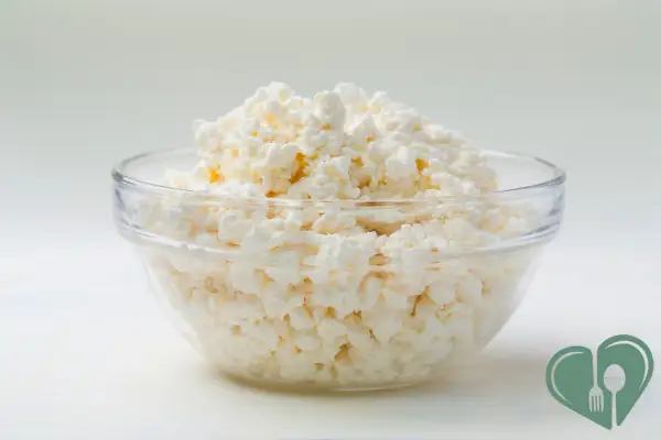 A glass bowl filled with plain cottage cheese, photographed against a light background