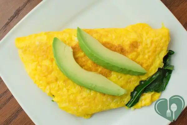 Simple veggie omelet with sautéed greens and sliced avocado on a white plat