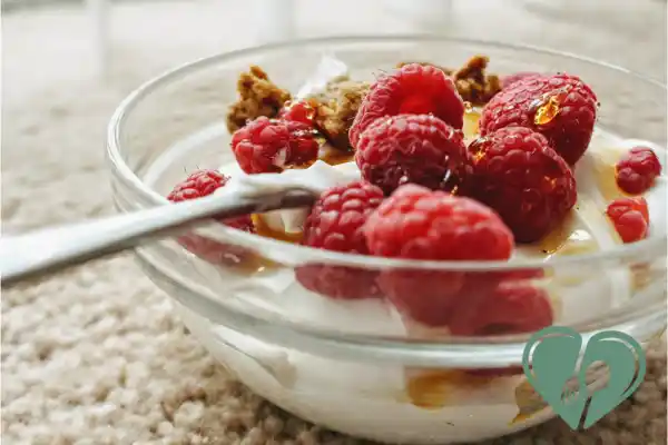 A glass bowl of plain Greek yogurt topped with fresh raspberries and a sprinkle of granola — a low-sugar, high-protein diabetic snack