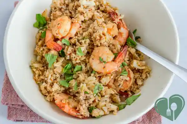 Low-carb shrimp stir-fry with cauliflower rice and herbs in a white bowl