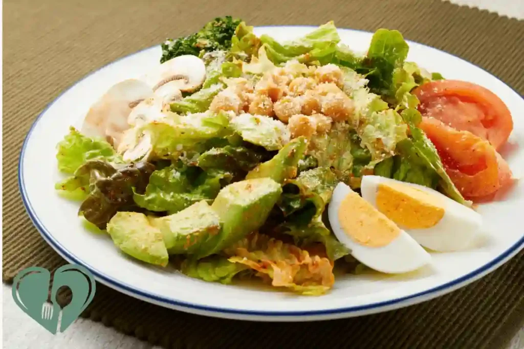 Boiled egg slices, leafy greens, avocado, chickpeas, tomato, and mushrooms on a white plate.