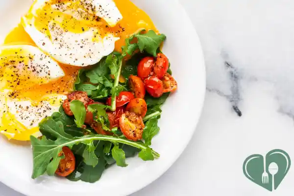 Soft-boiled eggs with cherry tomatoes and arugula on a white plate — a low-carb, high-protein diabetic breakfast.