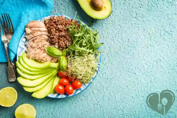 Balanced diabetic lunch plate with grilled chicken, quinoa, avocado, and fresh vegetables on a blue background