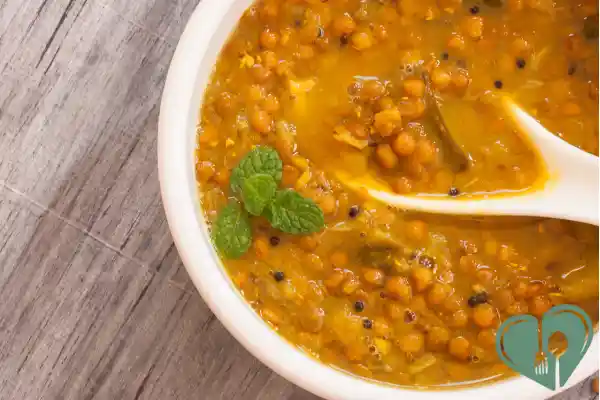 Warm lentil and tomato curry in a white bowl with a spoon and fresh mint