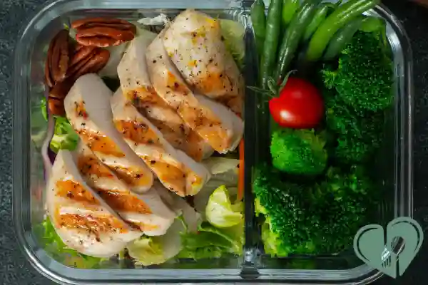 Diabetic meal prep container with grilled chicken, steamed broccoli, green beans, cherry tomato, and pecans on a bed of greens