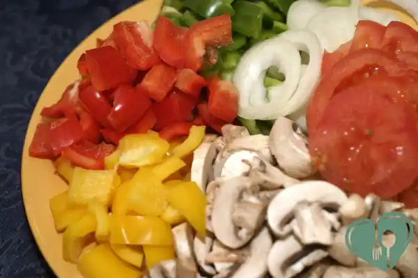 Freshly sliced low-carb pizza toppings: bell peppers, mushrooms, onions, and tomatoes on a yellow plate
