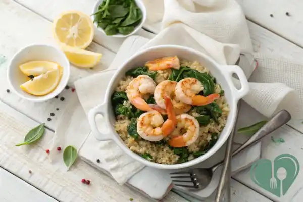 Grilled shrimp served over a bed of cooked quinoa and sautéed spinach in a white bowl on a rustic white background.