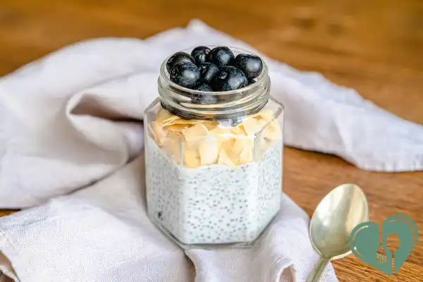 Glass jar of chia pudding topped with blueberries and coconut flakes on a wooden table.