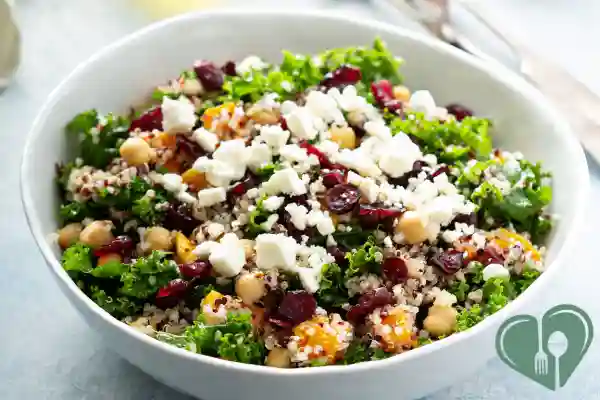 Kale, quinoa, and chickpea salad with dried cranberries and feta, served in a white bowl.
