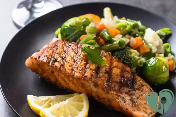 Grilled salmon fillet with steamed Brussels sprouts, broccoli, carrots, and lemon wedges