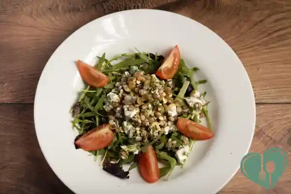 Lentil and feta salad on a bed of greens with tomato wedges, served in a white plate