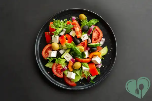Colorful Mediterranean salad with tomatoes, cucumbers, feta, olives, and greens on a black plate