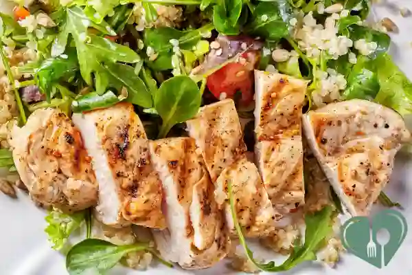 Grilled chicken breast served with mixed greens and quinoa on a white plate