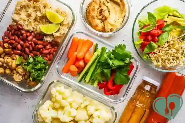 Glass containers filled with prepped low-carb vegetables, herbs, beans, and sauces arranged for healthy meal planning