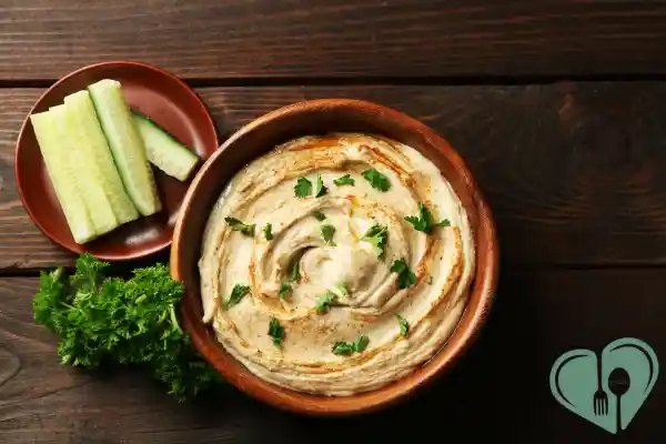 Cucumber sticks with hummus dip in a wooden bowl