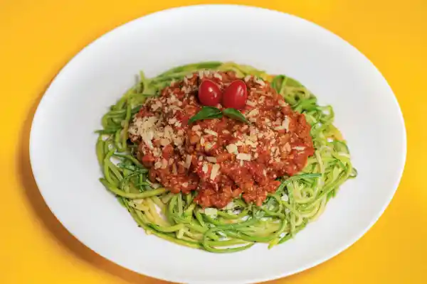 Zucchini noodles topped with tomato-based sauce and cherry tomatoes on a white plate