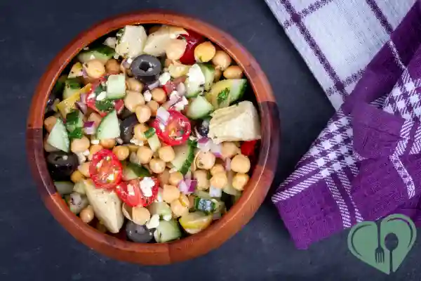 Chickpea salad with cherry tomatoes, olives, cucumbers, and feta in a wooden bowl
