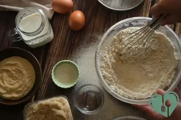 Person whisking low-carb flour in a bowl with baking ingredients on a wooden table