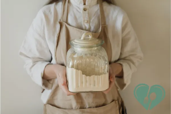 A woman in a neutral apron holding a sealed glass jar filled with low-carb flour — ideal storage for diabetic-friendly baking.