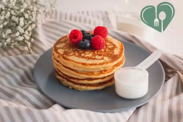 A stack of almond flour protein pancakes topped with raspberries and blueberries, served on a gray plate with a scoop of protein powder on the side — diabetic-friendly breakfast.