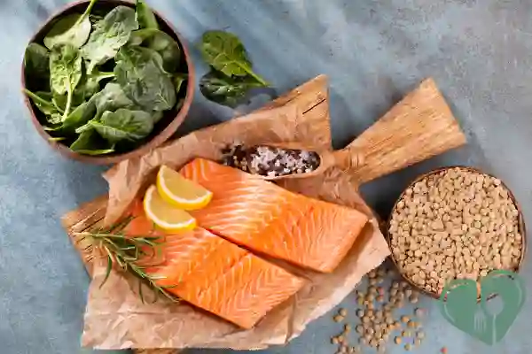 Raw salmon fillets with lemon slices, dry lentils, fresh spinach, and sea salt on a wooden board