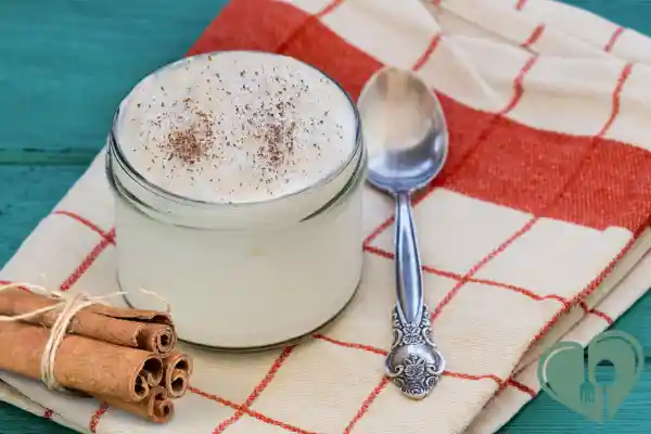 Glass jar of plain yogurt topped with cinnamon next to a spoon and cinnamon sticks