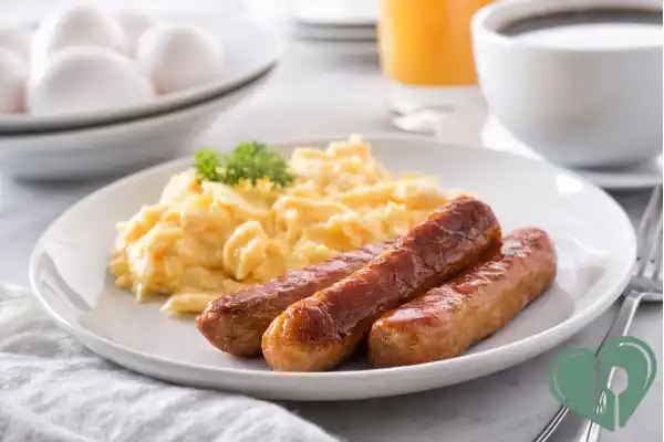 Plate with scrambled eggs and sausages served with coffee — a low-carb, high-protein diabetic breakfast.