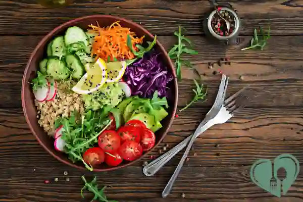 Colorful vegetarian diabetic dinner bowl with quinoa, avocado, tomatoes, cucumber, shredded carrot, and purple cabbage over greens