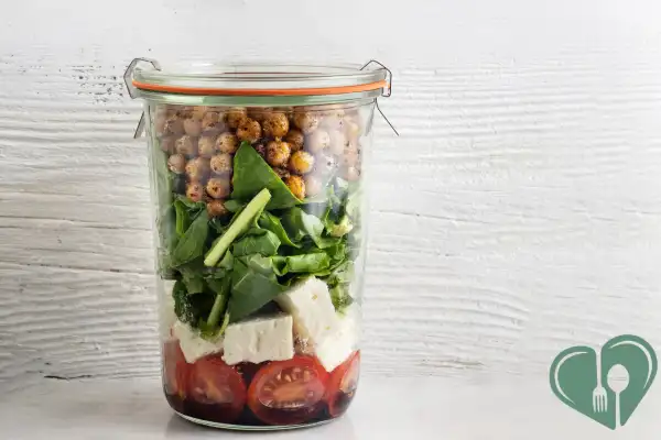 Layered mason jar salad with cherry tomatoes, feta cheese, spinach, and roasted chickpeas – perfect for a portable diabetic-friendly lunch.