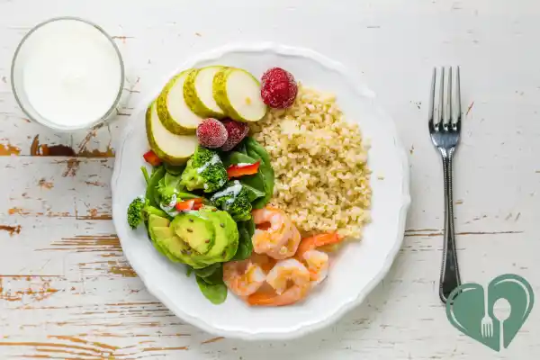 Diabetic-friendly portion plate with ½ vegetables and avocado, ¼ shrimp protein, and ¼ whole grains on a white wooden table