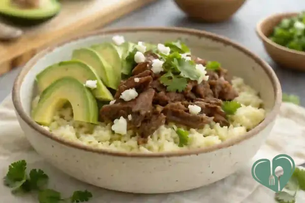 Low-carb beef and cauliflower rice bowl topped with avocado slices, feta, and cilantro - a high-protein, diabetic-friendly crockpot meal.