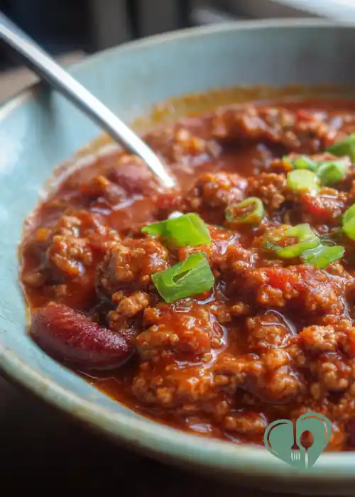 Close-up of chili with beans and lean ground beef in a ceramic bowl, topped with sliced green onions