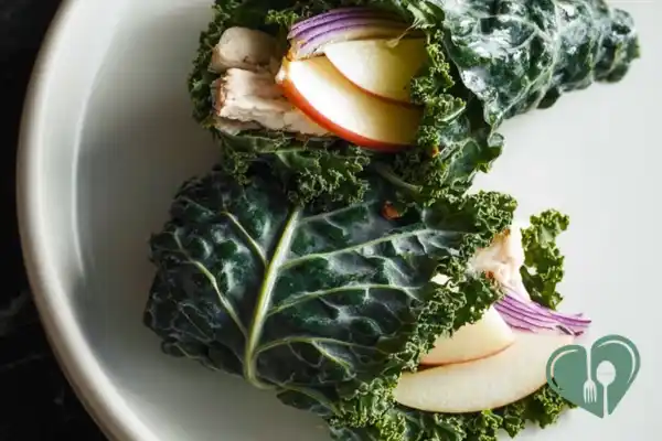 Close-up of chicken wraps with apple and kale cut in half on a plain plate
