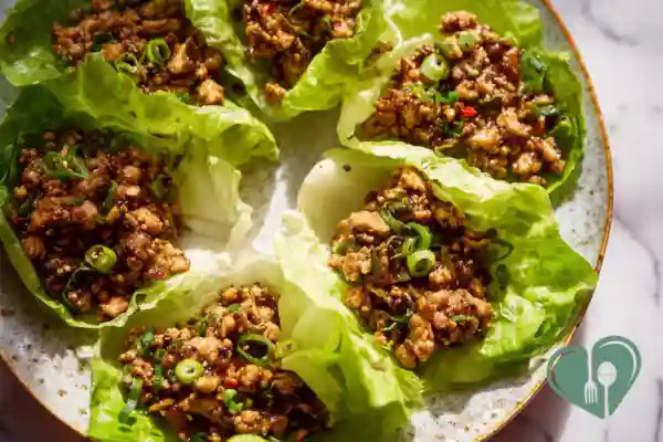 Close-up of chicken lettuce wraps folded with fresh greens on a plain plate