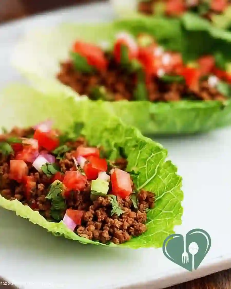 Two fresh taco lettuce wraps filled with seasoned meat and vegetables, served in crisp lettuce leaves.
