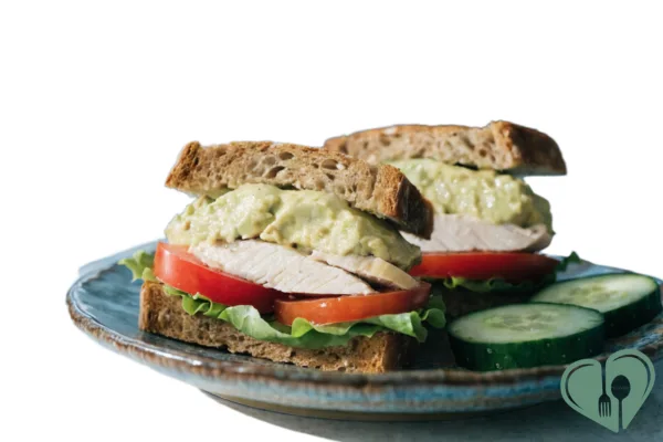 Avocado, tomato, and chicken sandwich on whole grain bread served with cucumber slices on a plate.